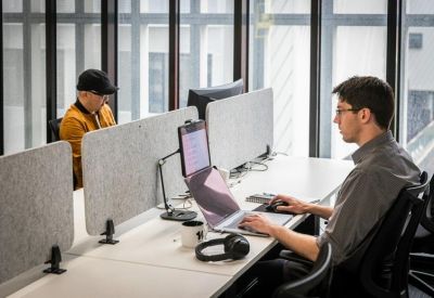 Modern workstations with grey privacy screens and people working on laptops.