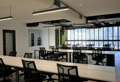 Spacious open-plan coworking area with white desks and black mesh chairs.