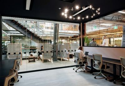 Shared workspace with glass partitions and views into a multi-level atrium.