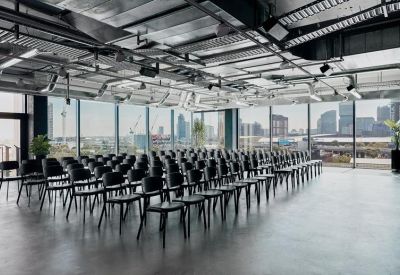 Large industrial-style event space with rows of black chairs and city views.