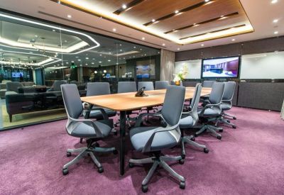Boardroom with a long wooden table, grey ergonomic chairs, and a wall-mounted screen.