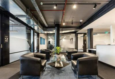 Spacious reception lounge with dark leather armchairs, glass coffee table, and exposed industrial ceiling.