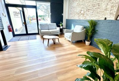 Light-filled lounge area with grey armchairs and a wooden coffee table near a glass entrance.