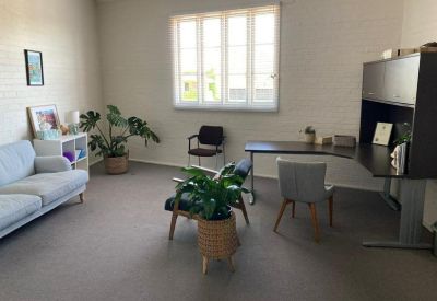Private office suite with a corner desk, grey sofa, and large window.