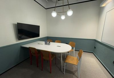 Private meeting room with a white oval table, colorful chairs, and a wall-mounted screen.
