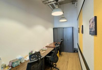Narrow workstation area with long wooden desks, ergonomic chairs, and industrial ceiling details.