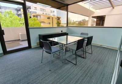 Bright glass-walled breakout room with a square table and views of the surrounding neighborhood.