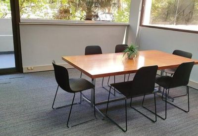 Casual meeting area with a wooden table, black chairs, and natural light from large windows.