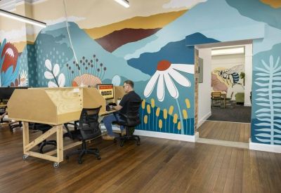 Open-plan workspace with wooden desks and a vibrant blue and gold mountain mural.