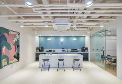 Modern office kitchen with a white island, bar stools, and a teal backsplash.
