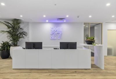 Modern white reception desk with neon branding, wooden floors, and potted palms.