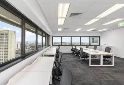 Light-filled workspace with several white desks and black mesh chairs.