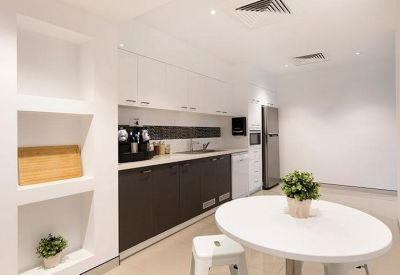 Bright, white communal kitchen and breakout area with a dining table and modern cabinetry.