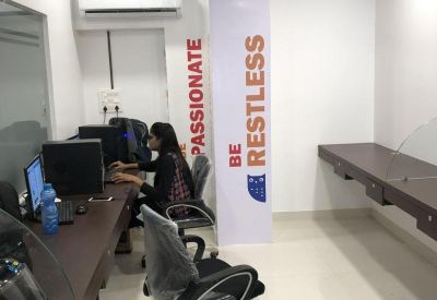 Office workspace with wall branding, ergonomic seating, and computer monitors on dark wood desks.