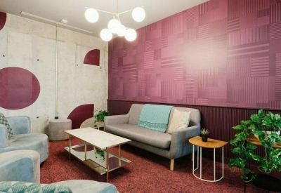 Cozy breakout room with a grey sofa, purple patterned wall, and potted greenery.