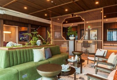 Reception lounge with a green tufted sofa, wooden coffee tables, and decorative bonsai plant.