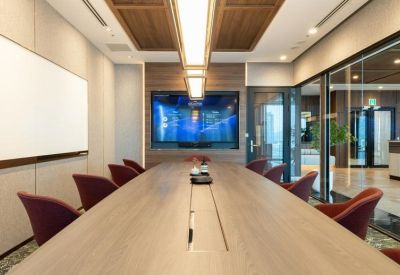 Conference room with a light wood table, red chairs, and a large wall-mounted display screen.