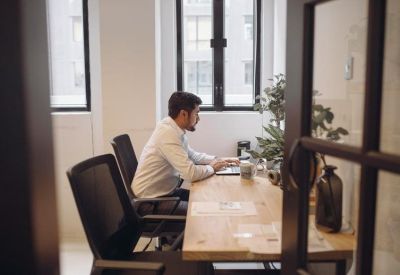 A professional working at a wooden desk in a bright private office suite.