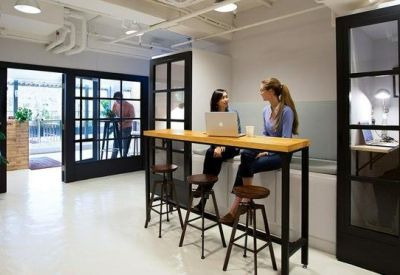 Bright indoor breakout area with high-top wooden tables and private phone booths.