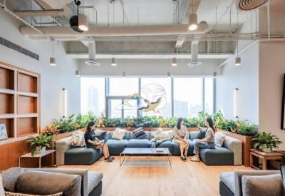 Modern open-plan lounge area with blue sectional sofas, indoor greenery, and industrial ceilings.