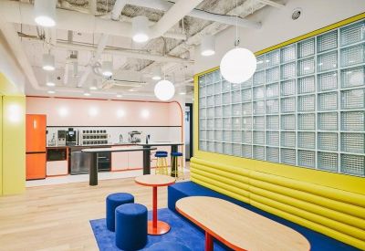 Kitchen breakout area featuring blue stools, a yellow ribbed wall, and glass block partition.