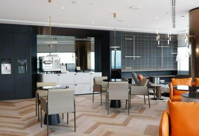 Sophisticated communal lounge and coffee bar featuring warm wood floors and orange leather armchairs.