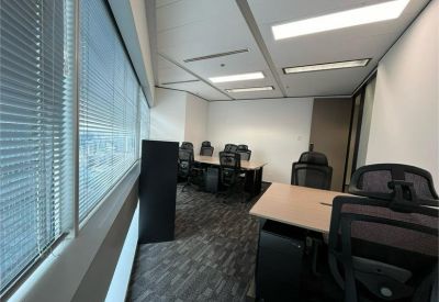 Linear office suite featuring multiple desks arranged along a window with blinds.