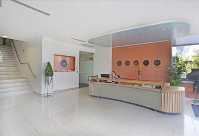 Bright reception area with a curved wooden desk, orange feature wall, and white tiled flooring.