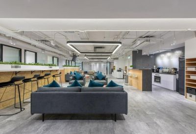 Open-plan coworking area with lounge seating and a kitchen in the background.