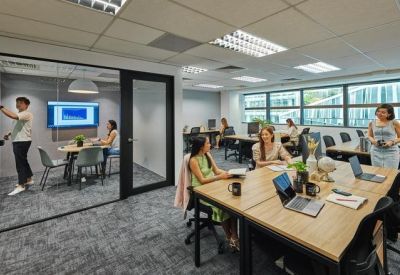 Open-plan office with wooden desks and a glass-enclosed collaboration room.