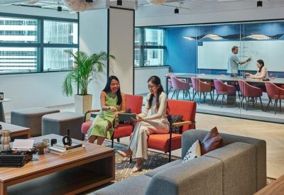 Bright lounge with orange armchairs and a glass-walled meeting room in the background.