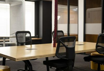 Coworking zone with a large light-wood table and black mesh ergonomic chairs.