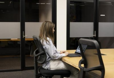 A professional working at a laptop in a private meeting room with glass walls.