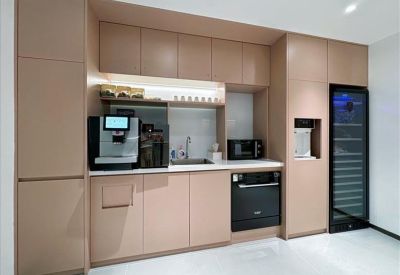 Sleek office kitchenette with light wood cabinetry, built-in microwave, and coffee machine.