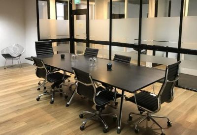 Spacious boardroom with a large black table, leather chairs, and frosted glass walls.