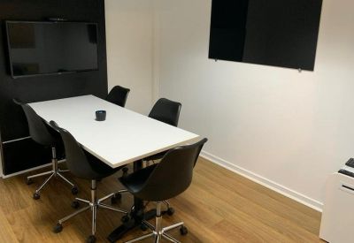 Small meeting room with a white table, four black chairs, and dual wall-mounted screens.