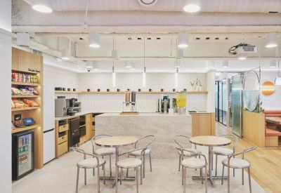 Bright office kitchen area with a marble island, café tables, and a snack pantry.
