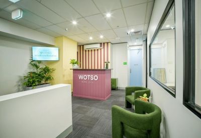 Modern reception area with a pink branded desk, green velvet armchairs, and striped wallpaper.
