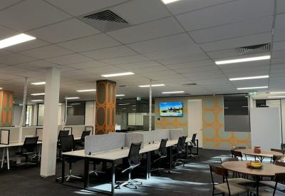 Large open-plan office space with rows of white desks, black chairs, and feature patterned pillars.