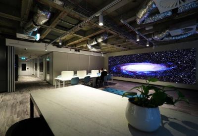 Sleek coworking area with a long white desk and a large space-themed digital wall display.