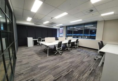 Modern open-plan workspace with white desks, ergonomic chairs, and large windows.