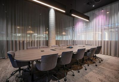 Professional boardroom with a long timber table, grey velvet chairs, and soft mesh curtains.