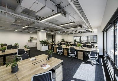 Modern open-plan office space with rows of wooden desks and black ergonomic chairs.