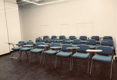 Lecture-style classroom with rows of blue chairs and folding desk arms.