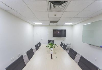 Modern conference room with a long table, ergonomic black chairs, and wall-mounted screen.