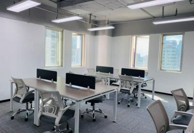 Open-plan office with multiple rows of desks, ergonomic chairs, and large windows.
