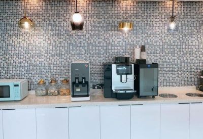 Communal kitchen area with coffee machine, microwave, and patterned tile backsplash.