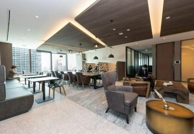 Sunlit lounge area featuring plush grey armchairs and several dining tables near a window.
