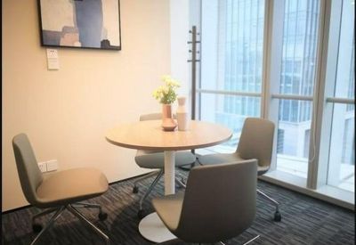 Small meeting area with a round wooden table and four grey chairs by a large window.