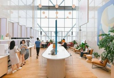 Bright, high-ceiling breakout area with a long white communal table and large window wall.